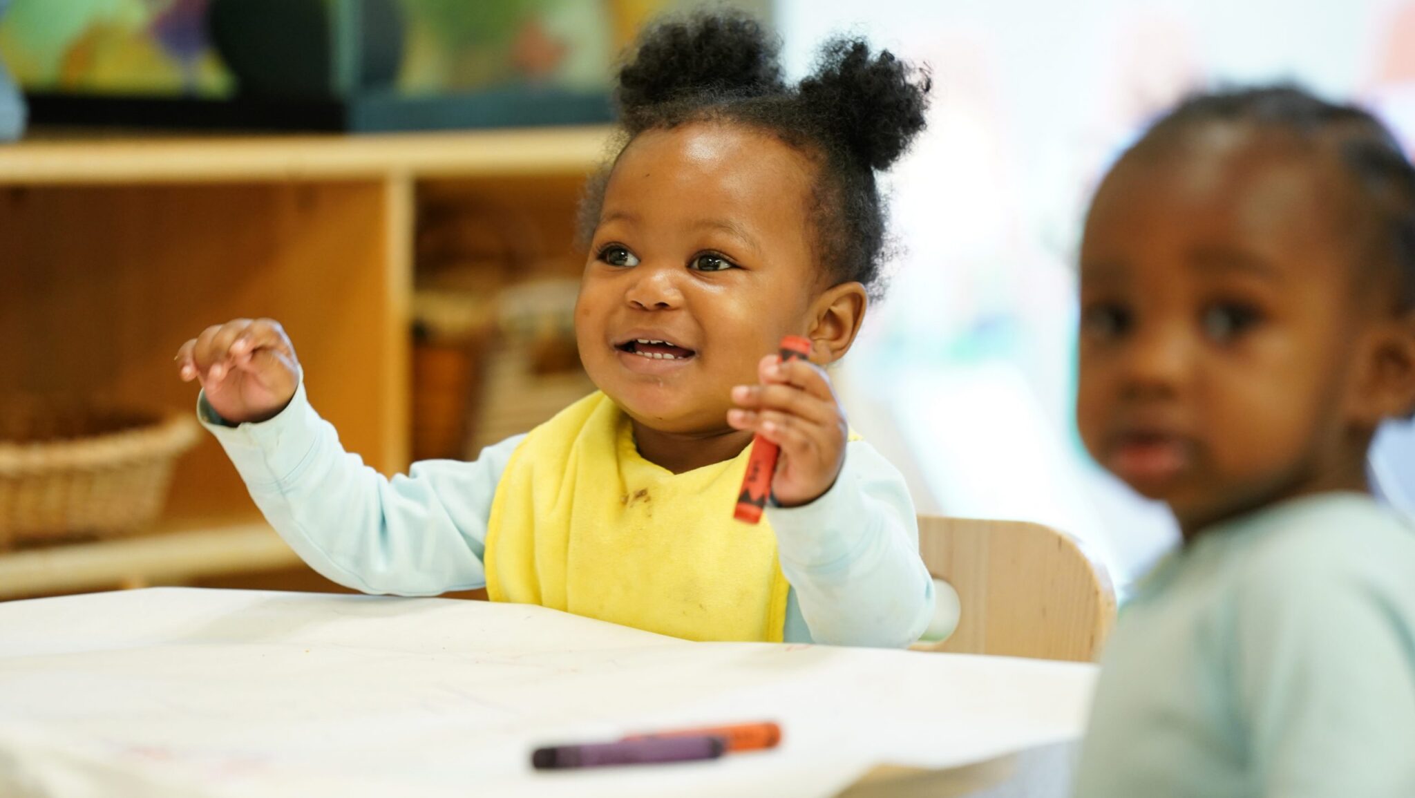 photo of two young children sitting at table with paper and crayons