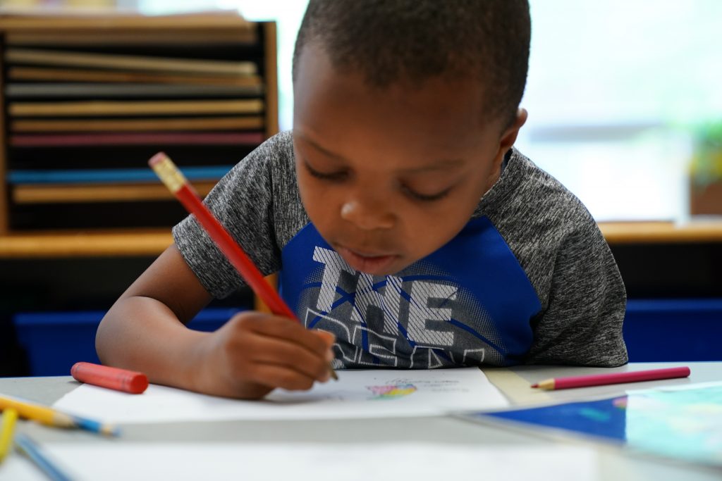 photo of child with drawing pencils sitting at table