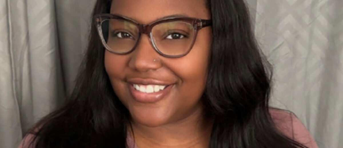 photo of Monique King smiling at camera with glasses on and a headband in her hair.