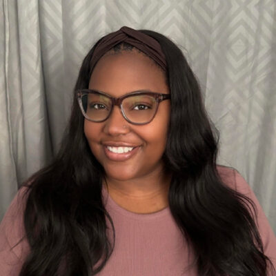 photo of Monique King smiling at camera with glasses on and a headband in her hair.